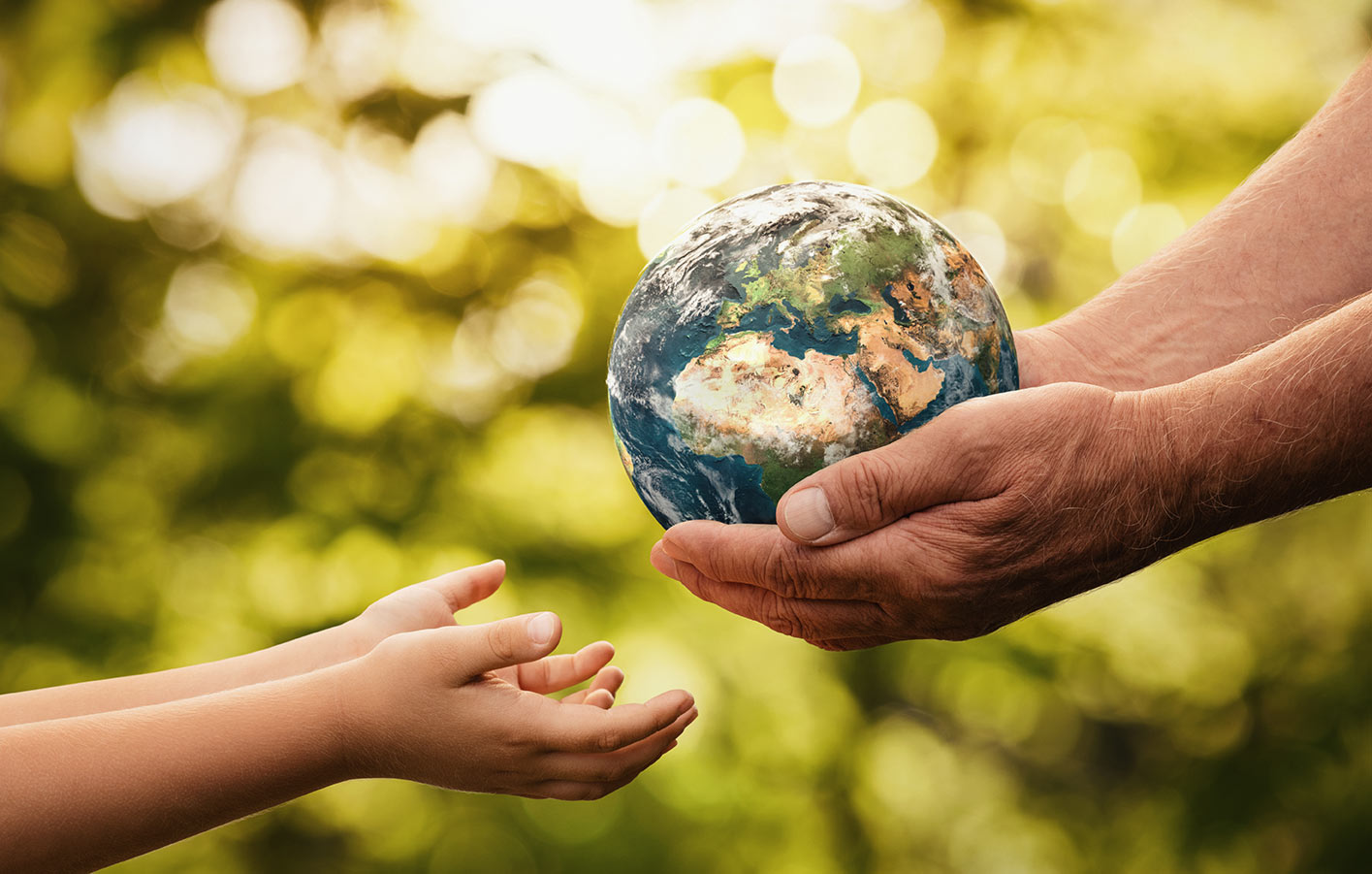 Hände eines Erwachsenen übergeben die Erde in die Hände eines Kindes vor einer grünen Waldlandschaft.